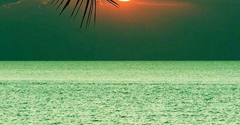 صورة اغروب الشمس من خلف السحب فوق مياه البحر الزرقاء في منظر جميل جدا